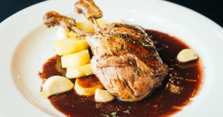 Cuisse de canard confite laquée dans une sauce rouge, servie avec des pommes de terre et de l'ail.